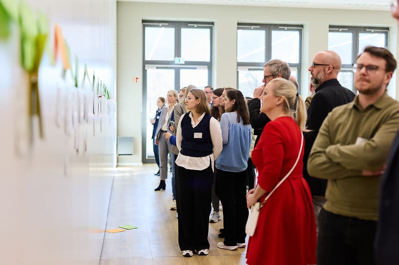 Menschen lesen beschriftete Klebezettel, die an der Wand kleben.