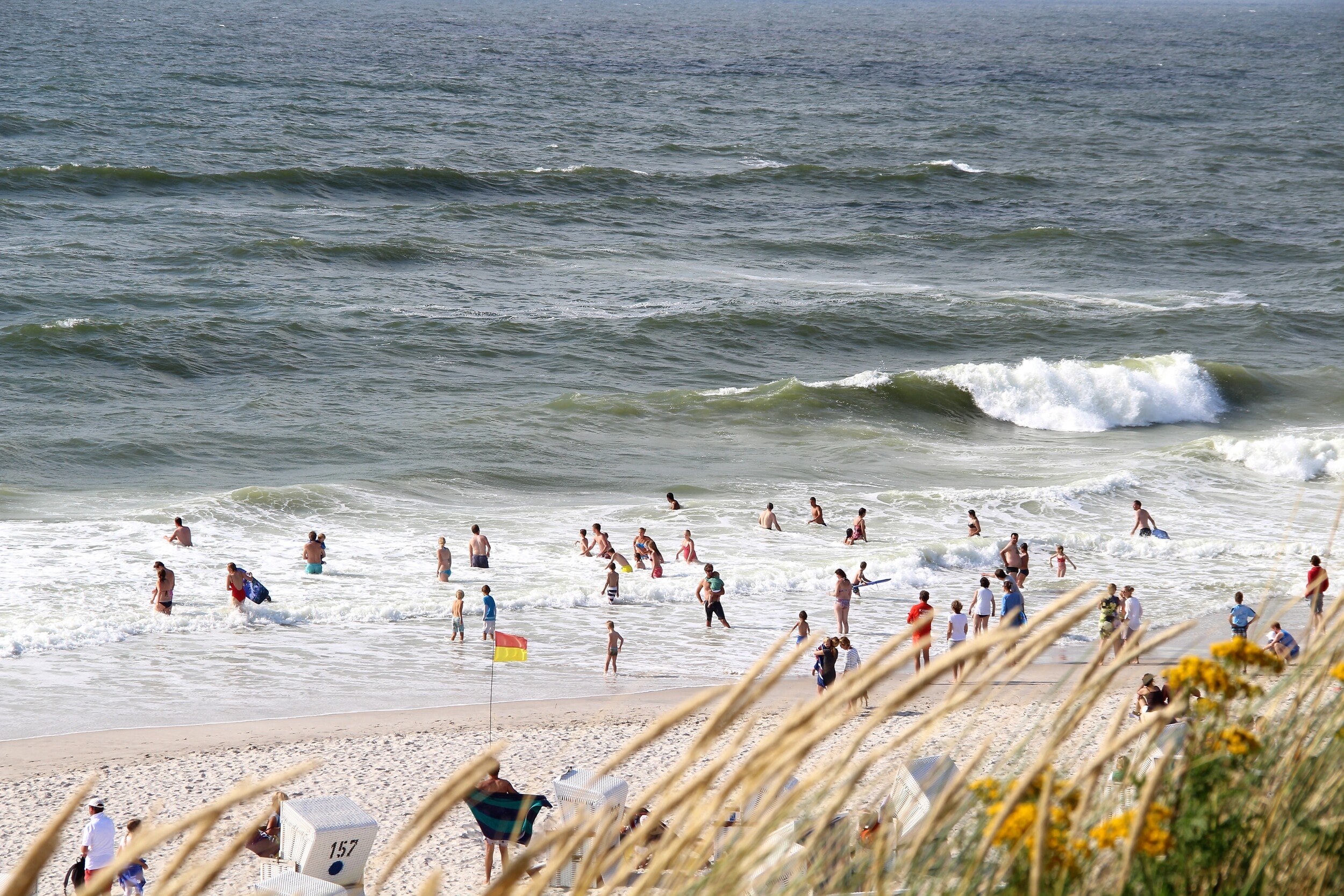 Menschen baden in den Wellen vor dem Sandstrand von Sylt im Sommer. 