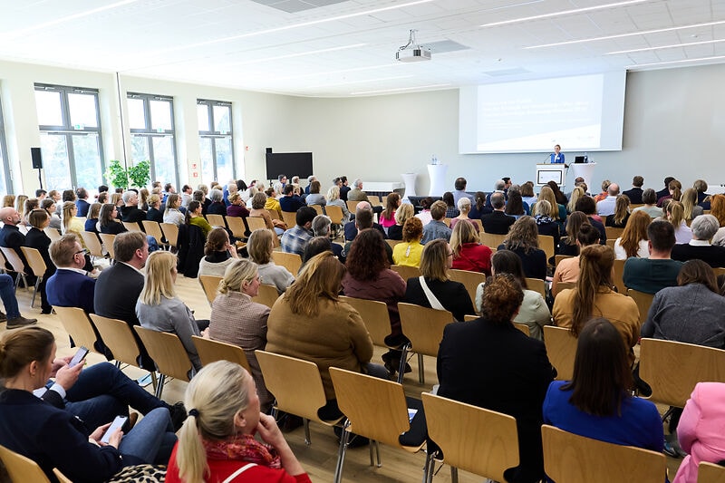 Rednerin am Rednerpult auf der Bühne vor Publikum