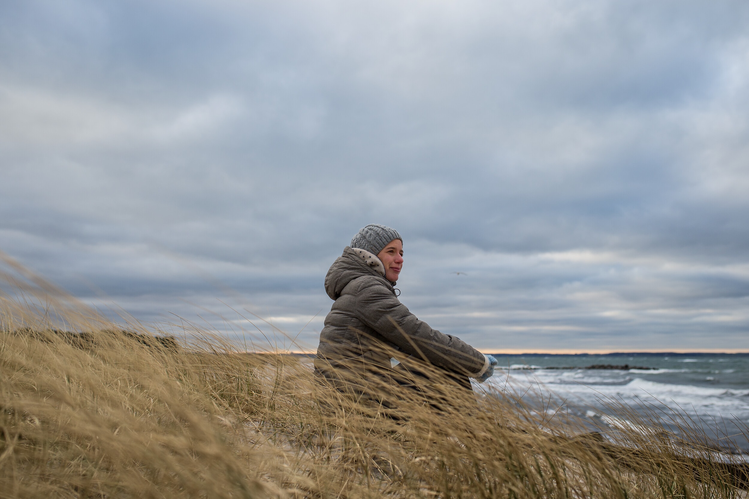 Frau in Winterjacke und Mütze blickt auf das Meer am Schönberger Strand