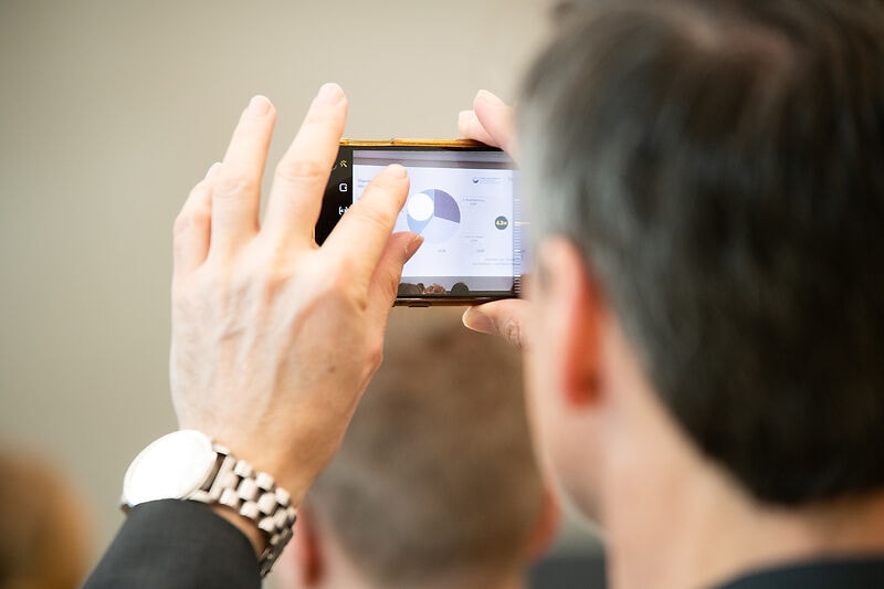Ein Mann fotografiert ein Diagramm von einer Leinwand mit seinem Handy.