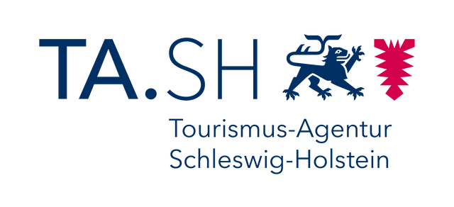 Logo der „TA.SH Tourismus-Agentur Schleswig-Holstein“: dunkelblauer Schriftzug „TA.SH“, darunter „Tourismus-Agentur Schleswig-Holstein“, rechts ein blauer Löwe und daneben ein rotes Nesselblatt.